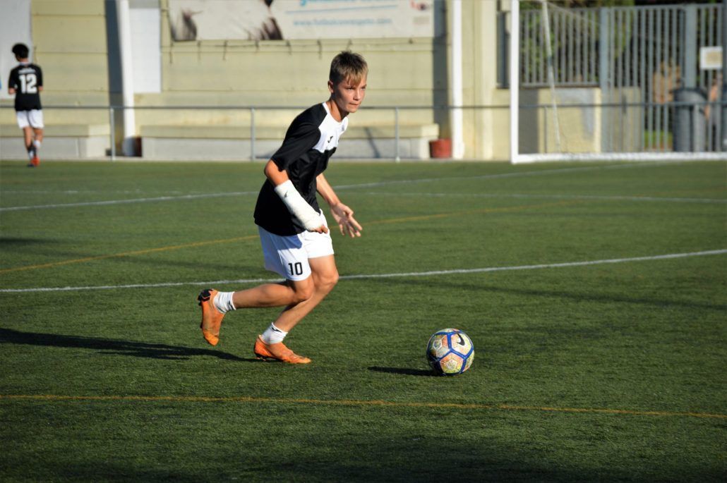 A young man is kicking a soccer ball on a field.