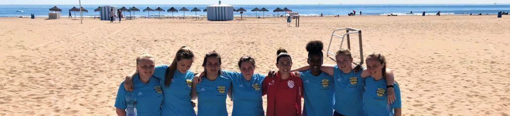 A group of girls are posing for a picture on a beach after completing a beach soccer session