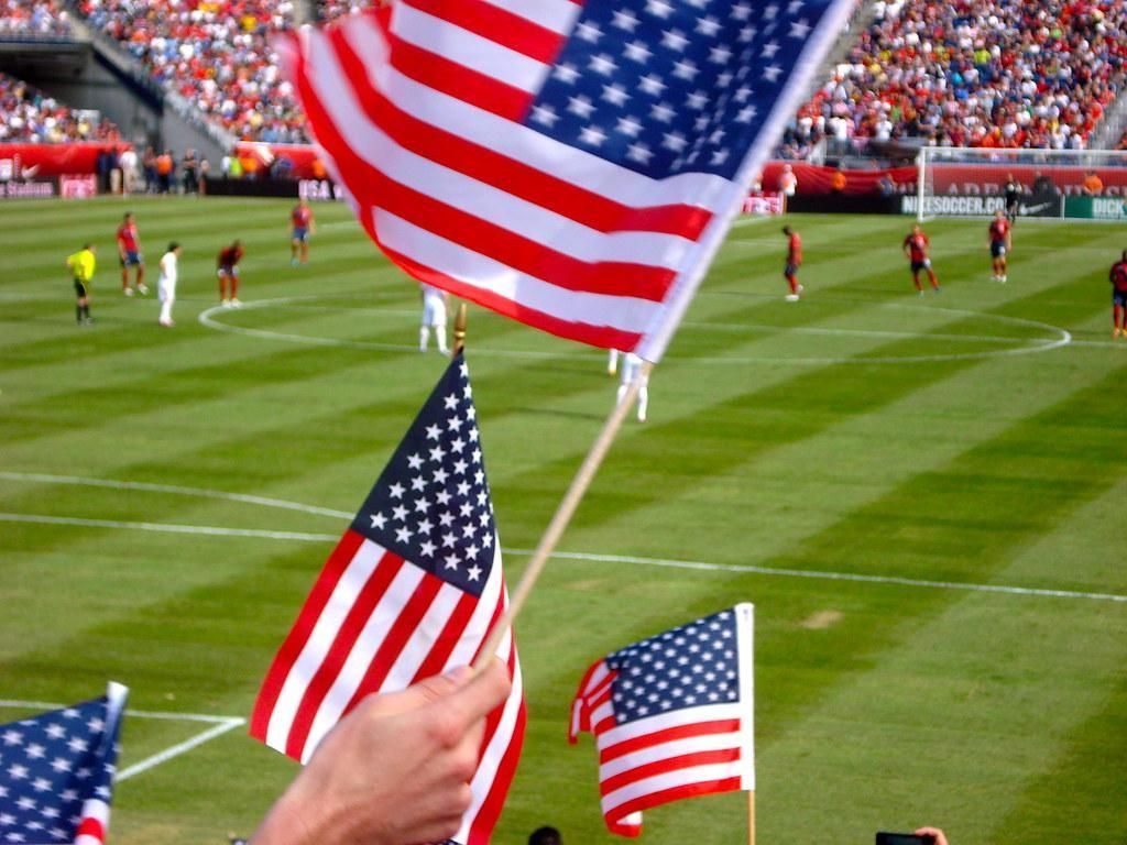 A person holding an american flag in front of a soccer field