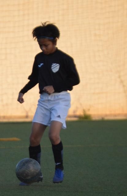 A young boy in a black shirt and white shorts is kicking a soccer ball