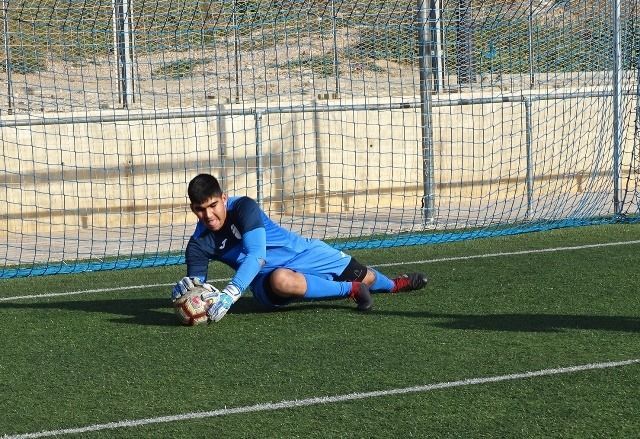 A soccer goalie is kneeling down to catch a soccer ball.