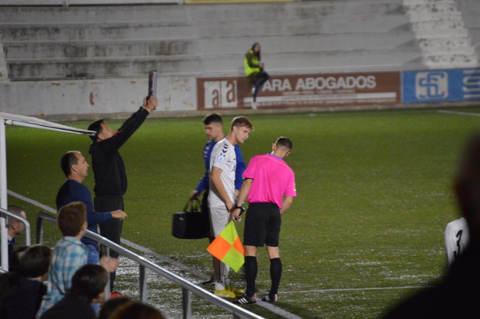 A group of men are standing on a soccer field with an ad for ara abogados in the background