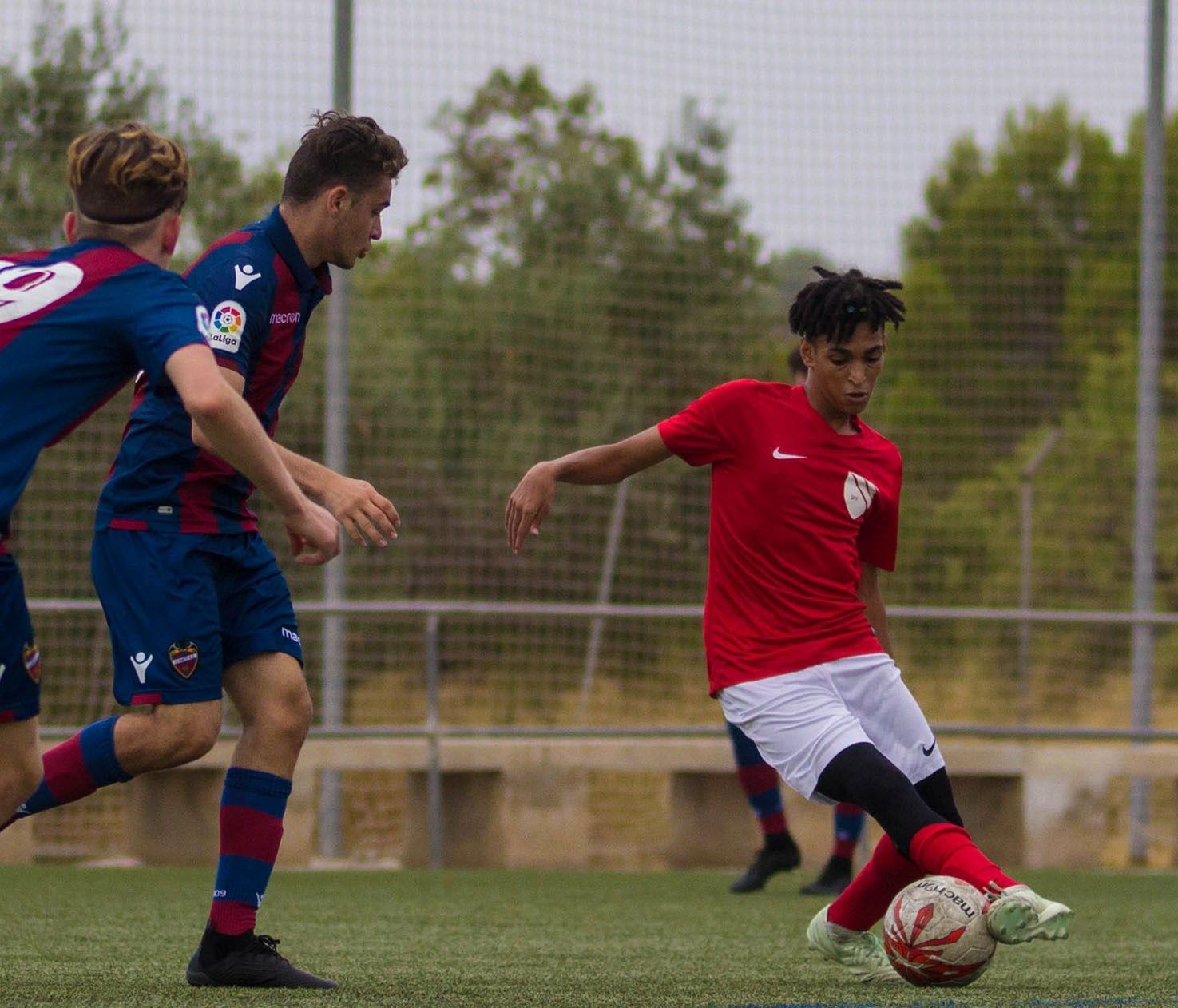 A man in a red shirt is kicking a soccer ball