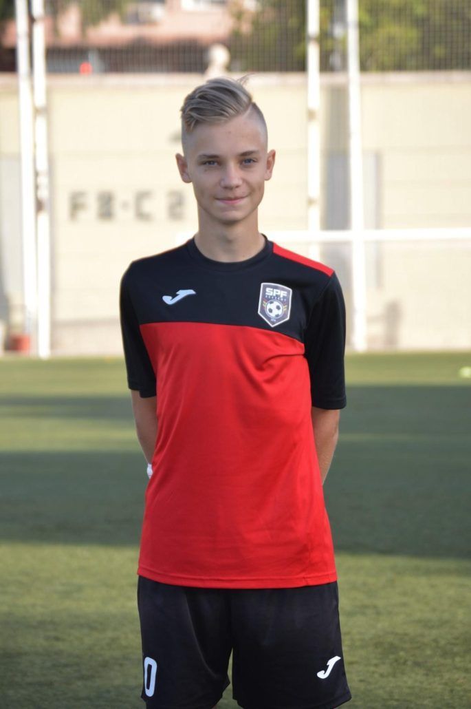 Yarik in a red and black soccer uniform is standing on a field.