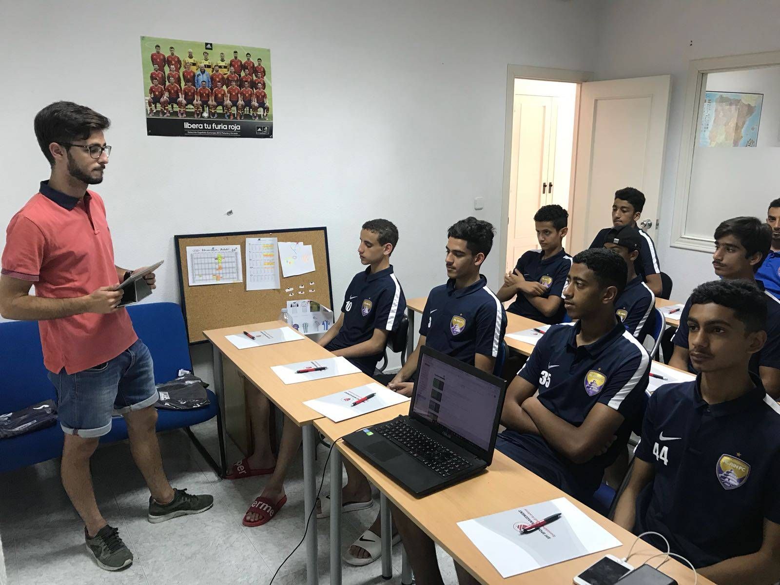 A man is giving a presentation to a group of young soccer players in a classroom.