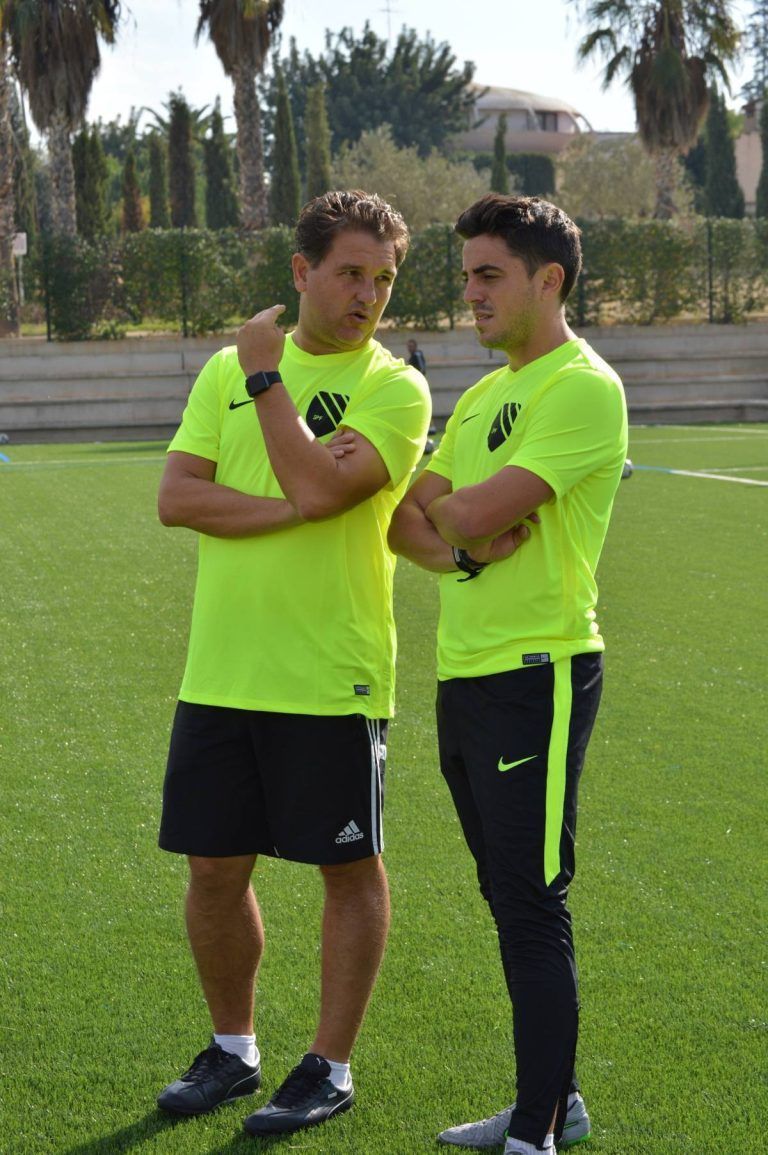 Two coaches are standing next to each other on a soccer field.