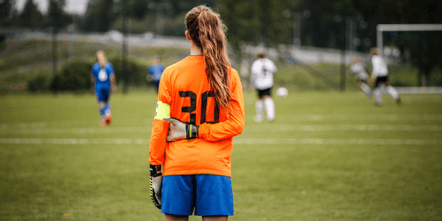 A female soccer player in a goalkeeper jersey is standing on a soccer field.