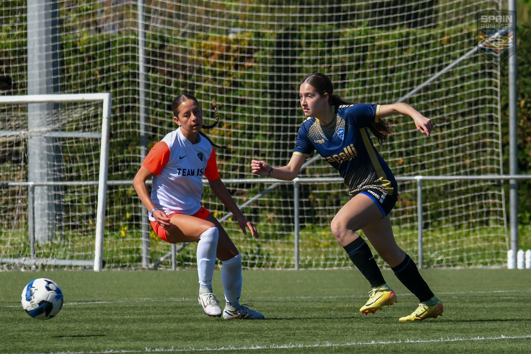 Two female soccer players are playing a game of soccer on a field.