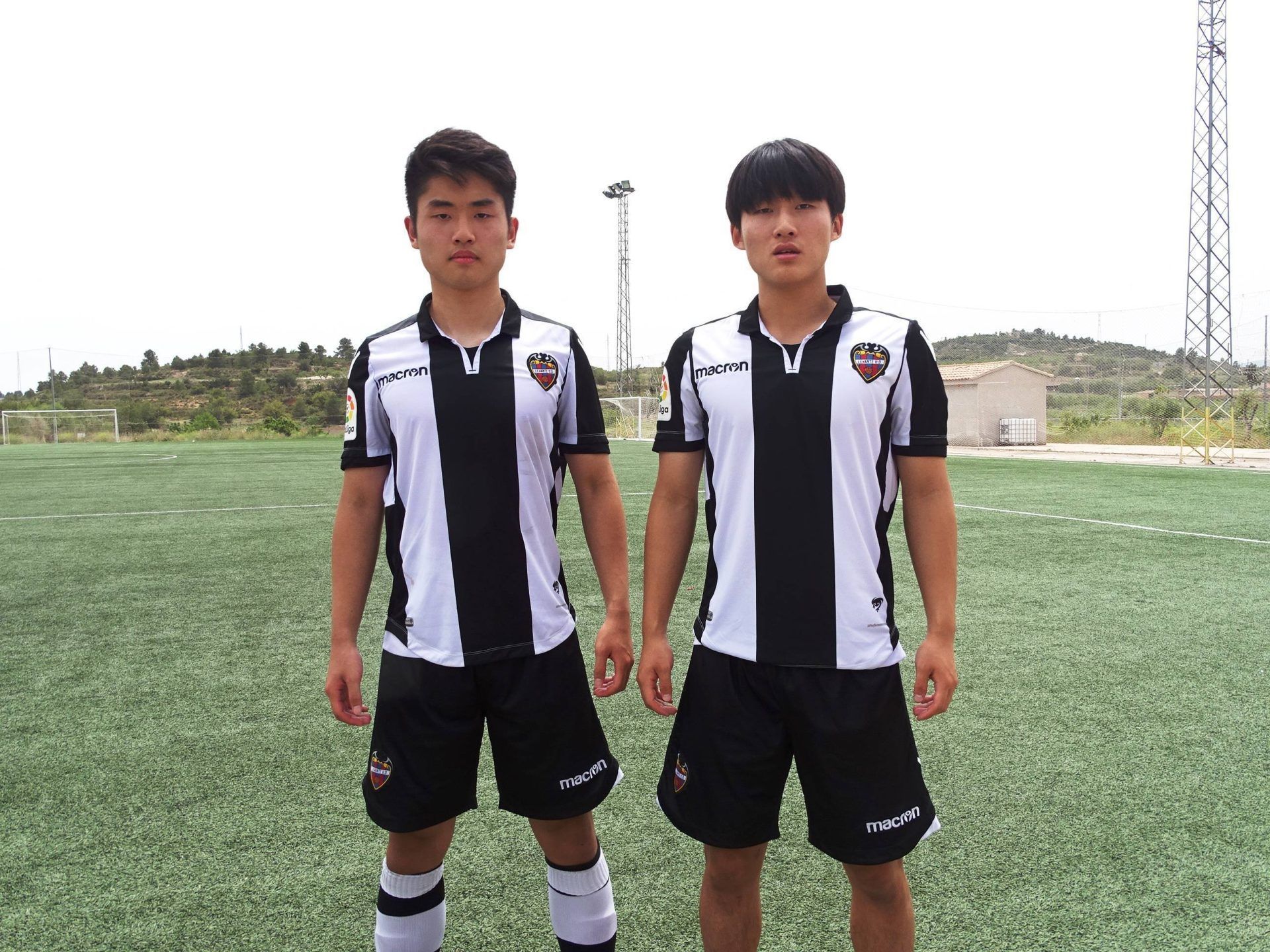 Two young men are standing next to each other on a soccer field.