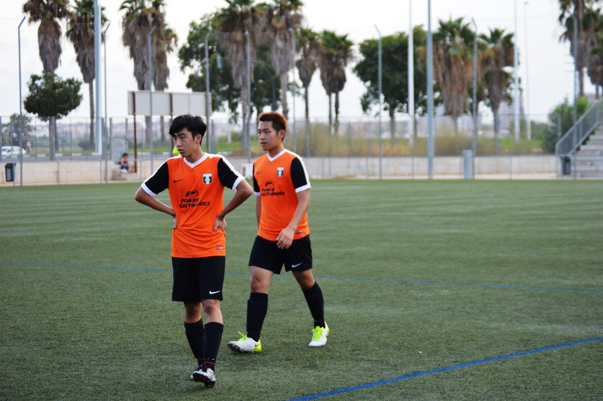 Two soccer players are standing on a field with their hands on their hips.