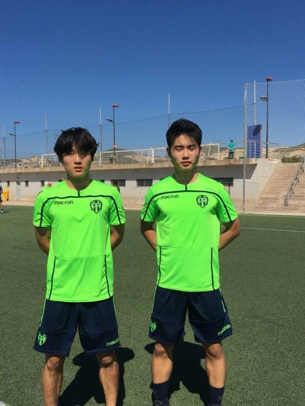 Two soccer players standing on a field wearing green shirts