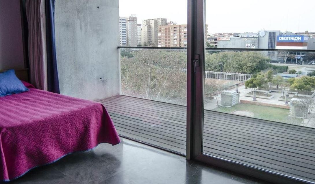 A bedroom with a bed and a balcony with a view of a city.