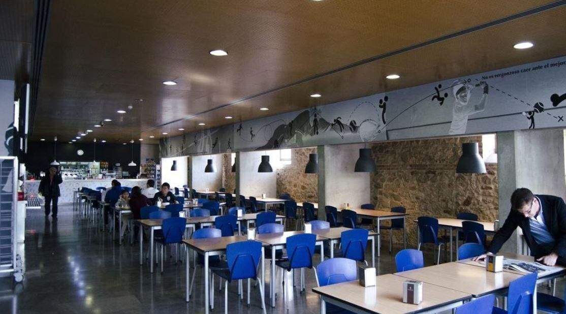 A man is standing at a table in a restaurant with tables and chairs.