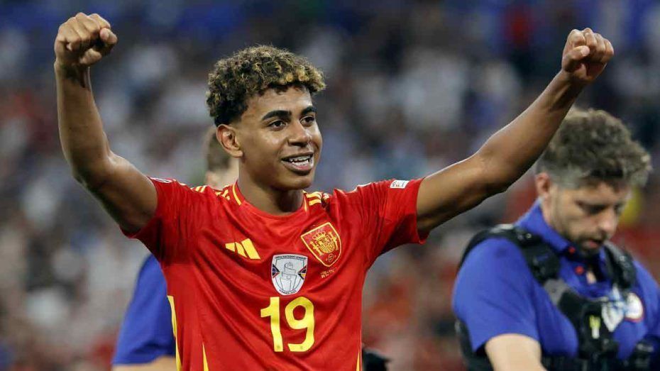 Lamine Yamal wearing a red jersey with the number 19 on it is raising his arms in the air.