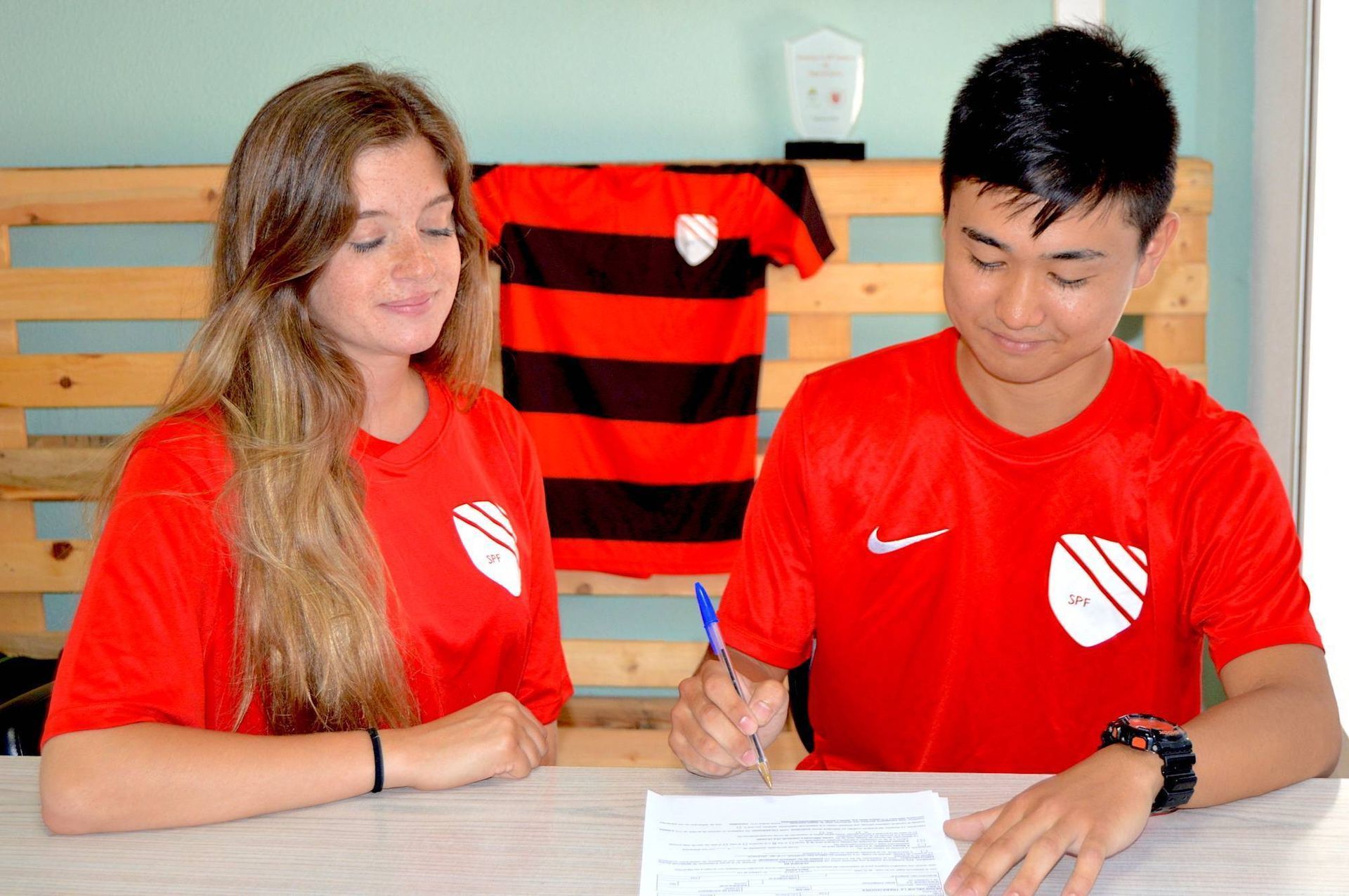 Mahiro Hasegawa and a woman are sitting at a table signing a document.