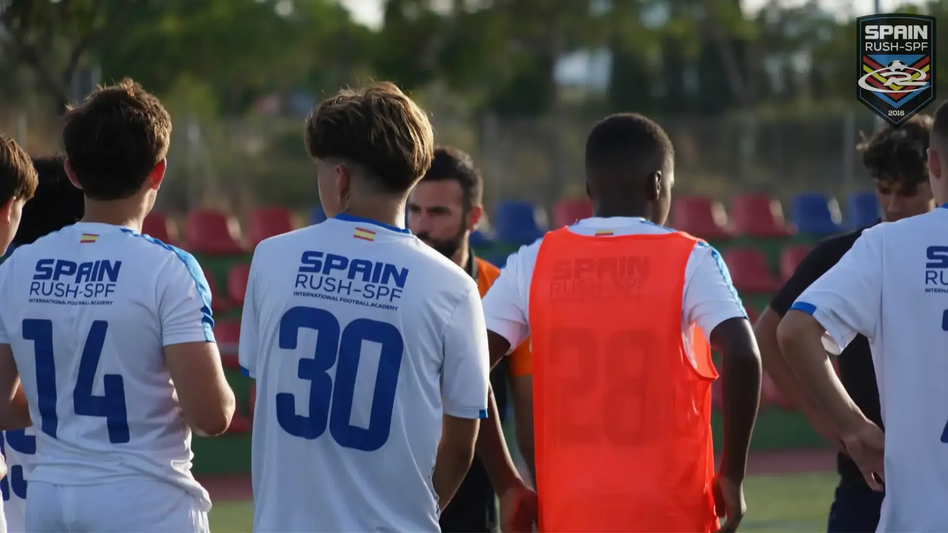 Spain Rush SPF players standing on a soccer field listing to their coach during a soccer tryout