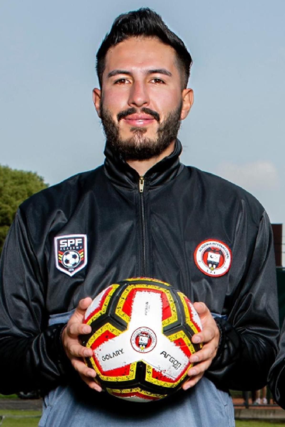 Miguel Angle Rodriguez in a black jacket is holding a soccer ball