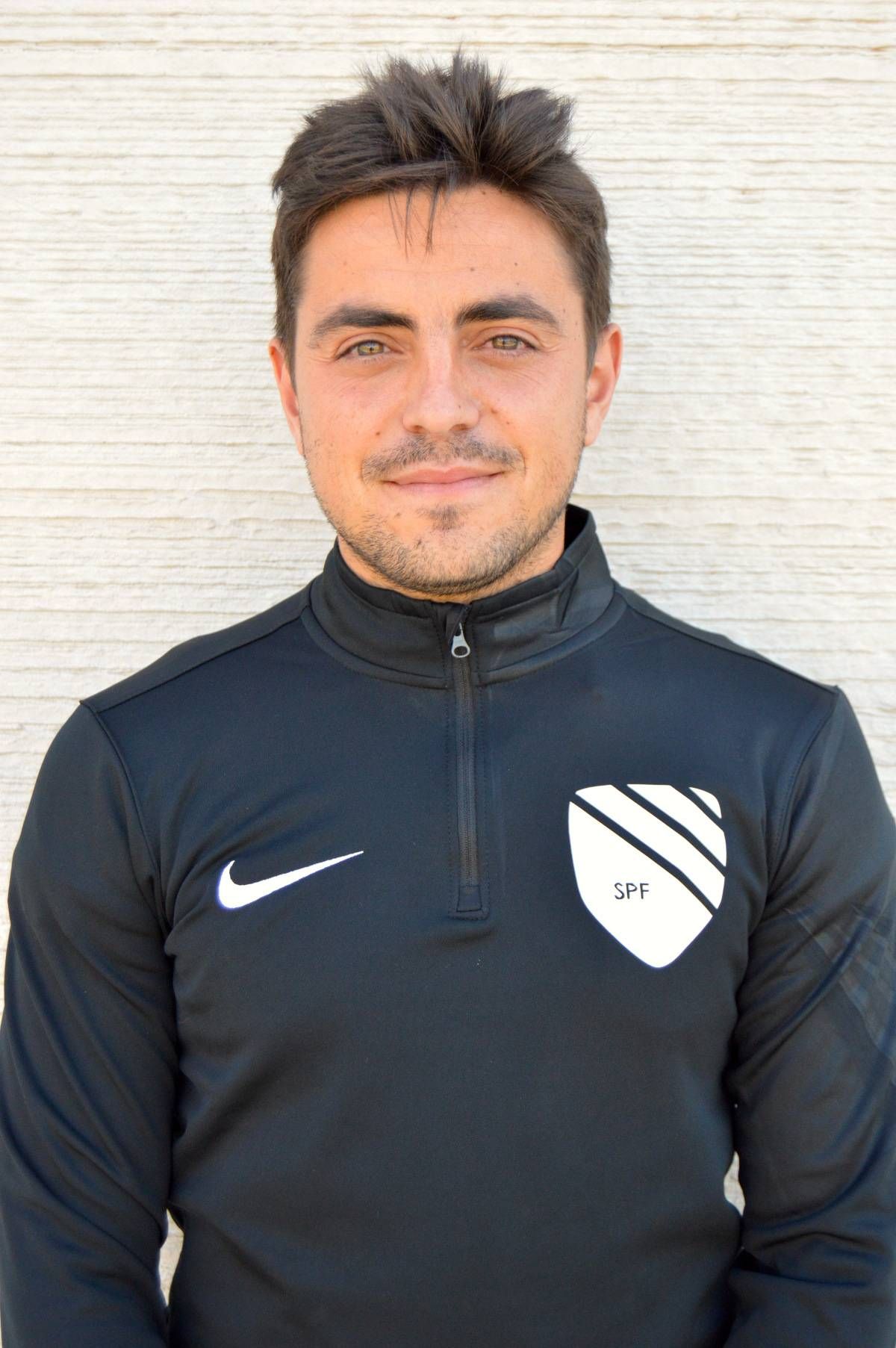 A man wearing a black nike sweatshirt is standing in front of a white wall.