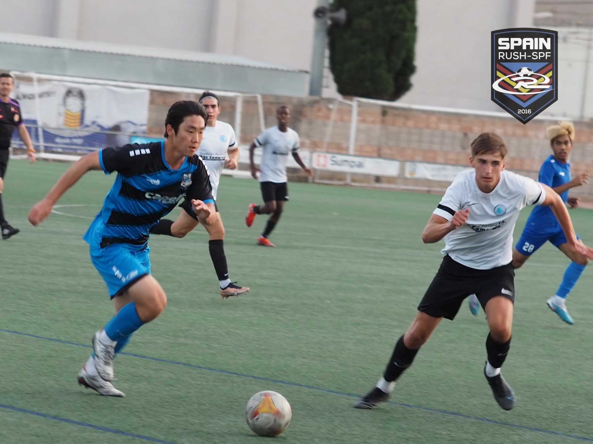 A group of young men are playing soccer on a field sponsored by spain rush