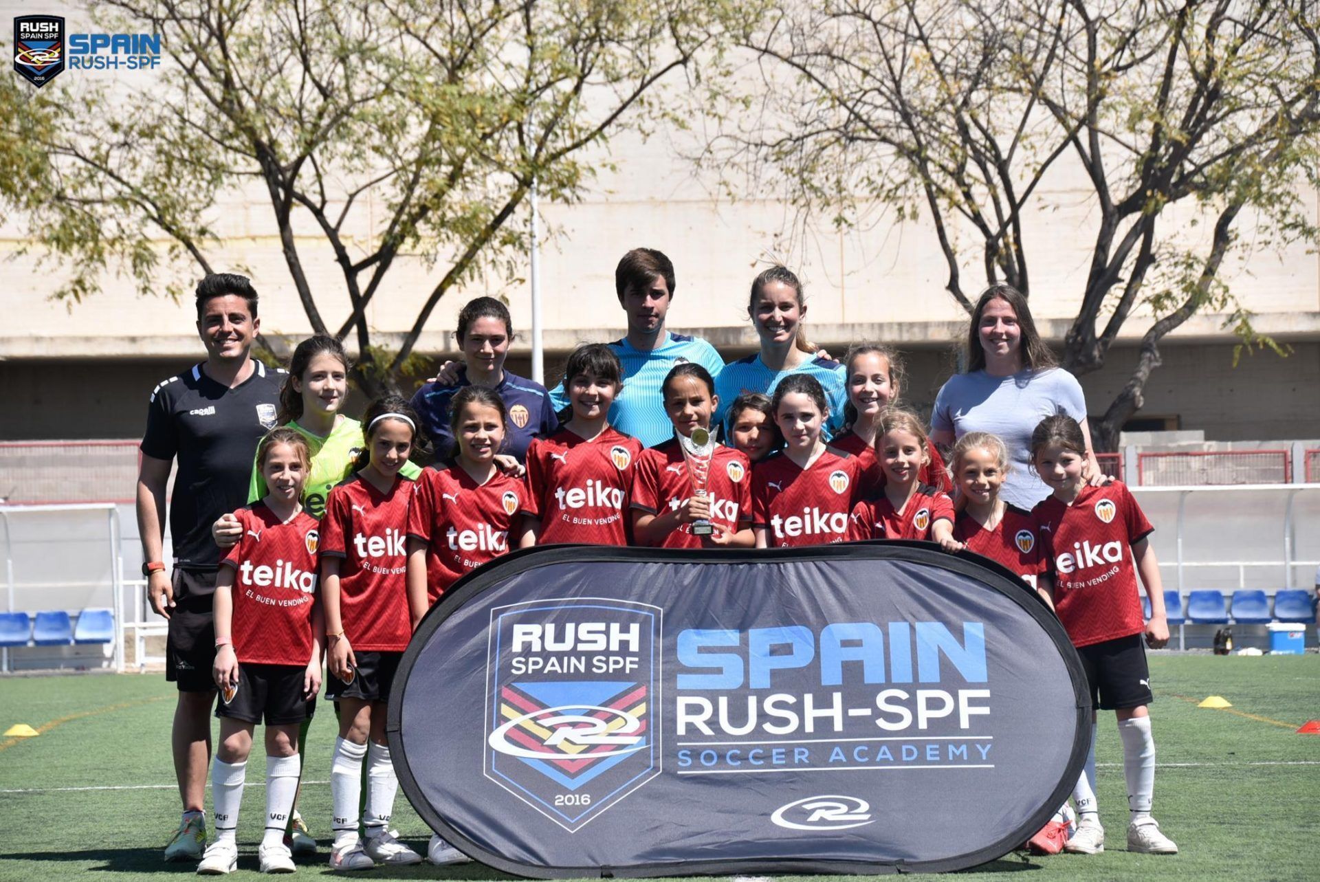 A group of young girls are posing for a picture in front of a banner that says spain rush spf soccer academy.