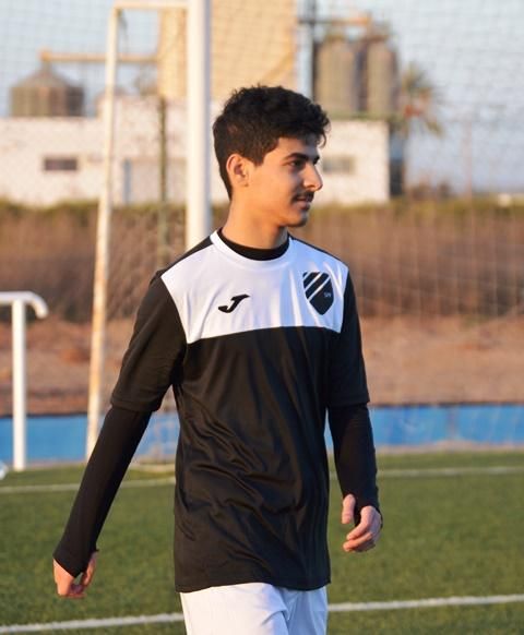 A Swiss young man wearing a black and white joma shirt walks on a soccer field