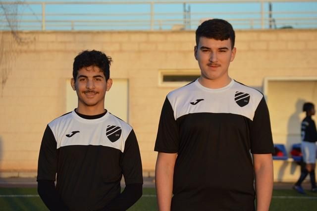 Two young men are standing next to each other on a soccer field