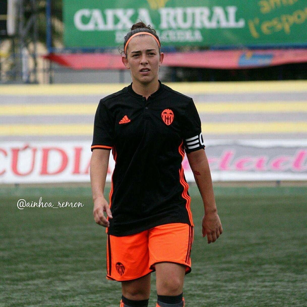 A female soccer player stands on a field in front of a sign that says caixa rural