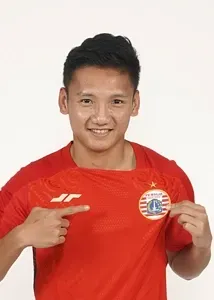 Syahrian Abimanyu in a red soccer jersey is pointing at his shirt.