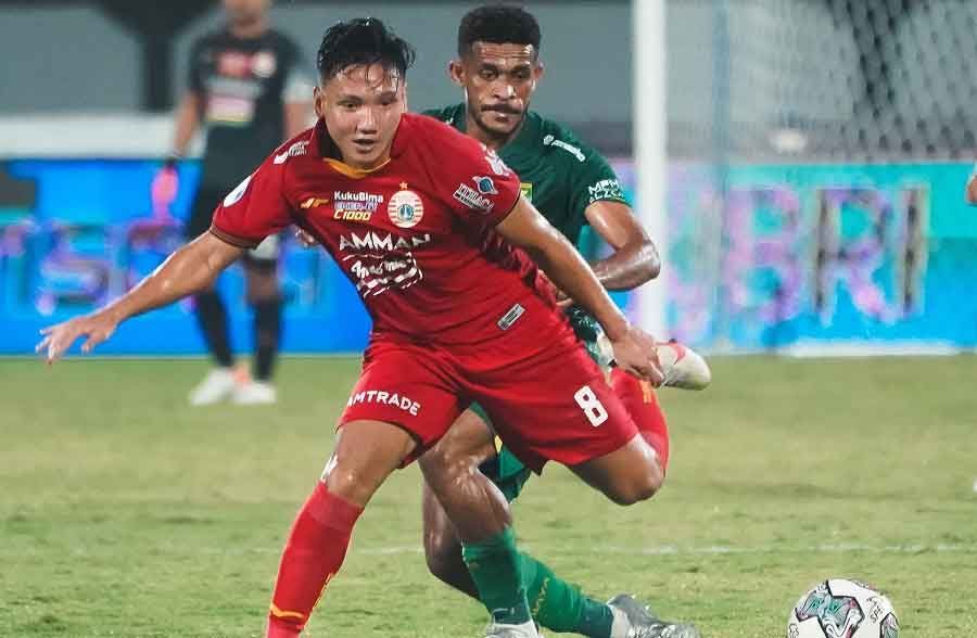 Syahrian Abimanyu dribbling a soccer ball with a defender in a green uniform behind him