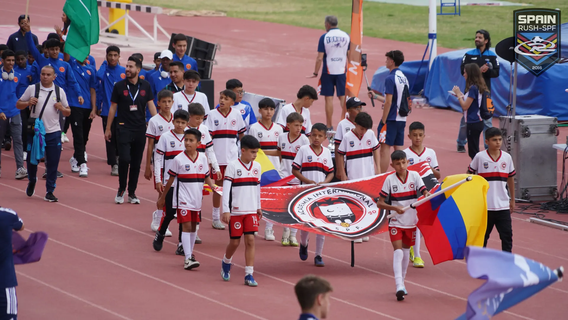 A group of young boys are walking down a track holding flags.