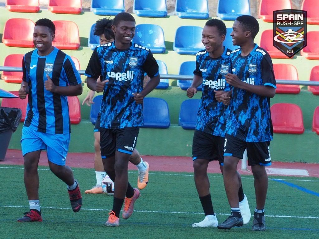 A group of Spain Rush SPF players from Africa are running on a soccer field.