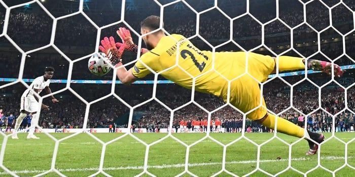 A soccer goalkeper is diving to catch a soccer ball in the net.