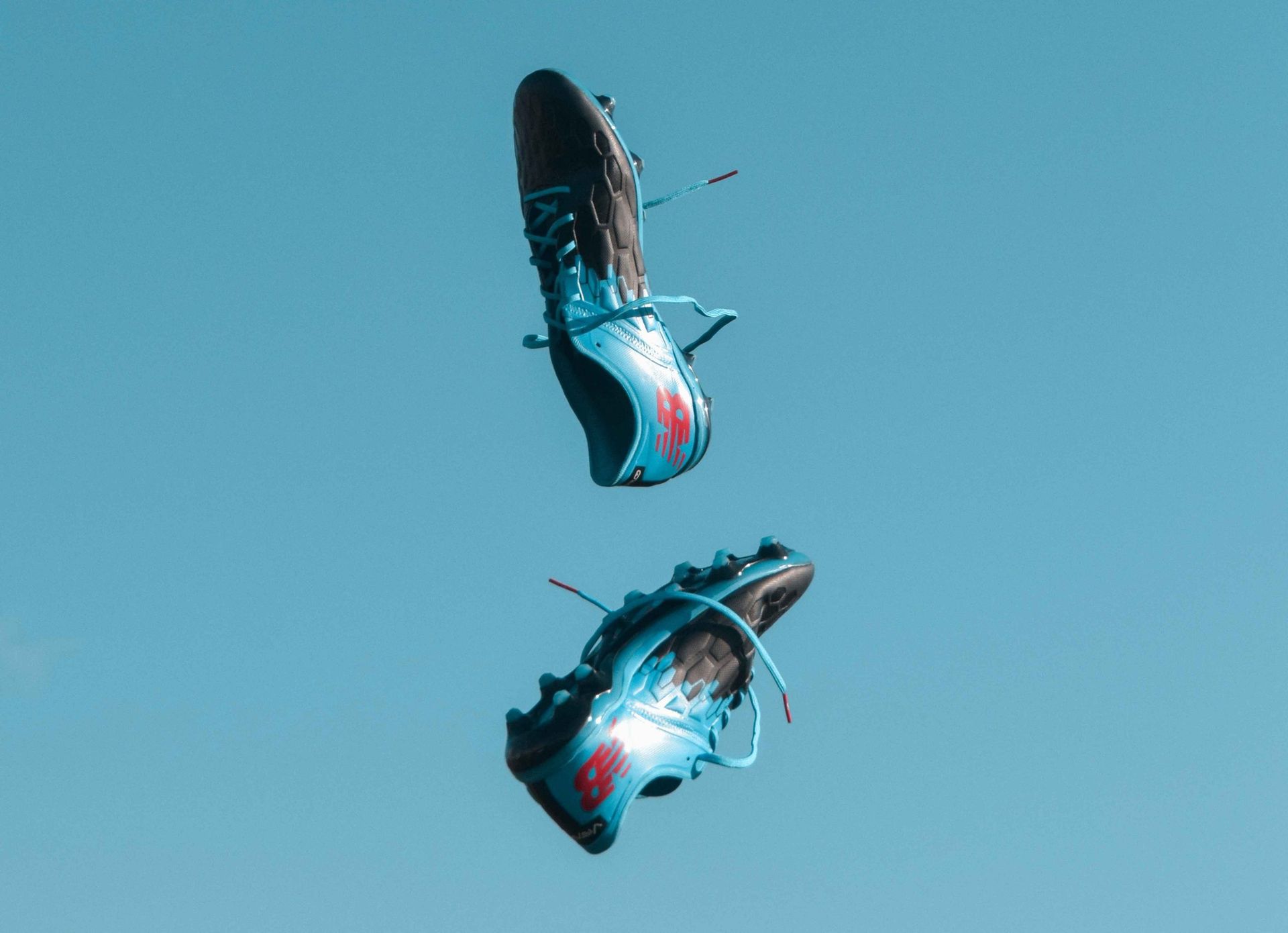 blue soccer cleats in the air with a blue sky background