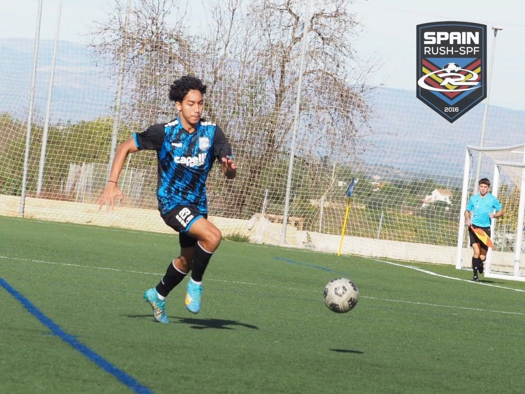 A young boy is running after a soccer ball on a field.