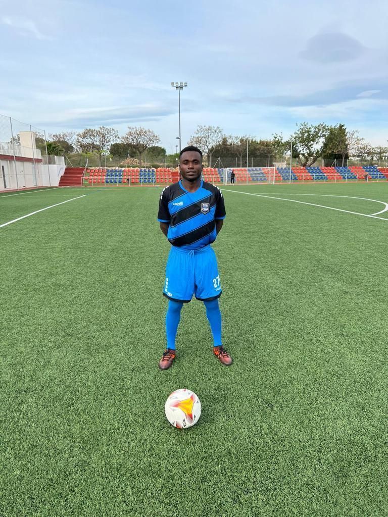 A young man is standing on a soccer field with a soccer ball.