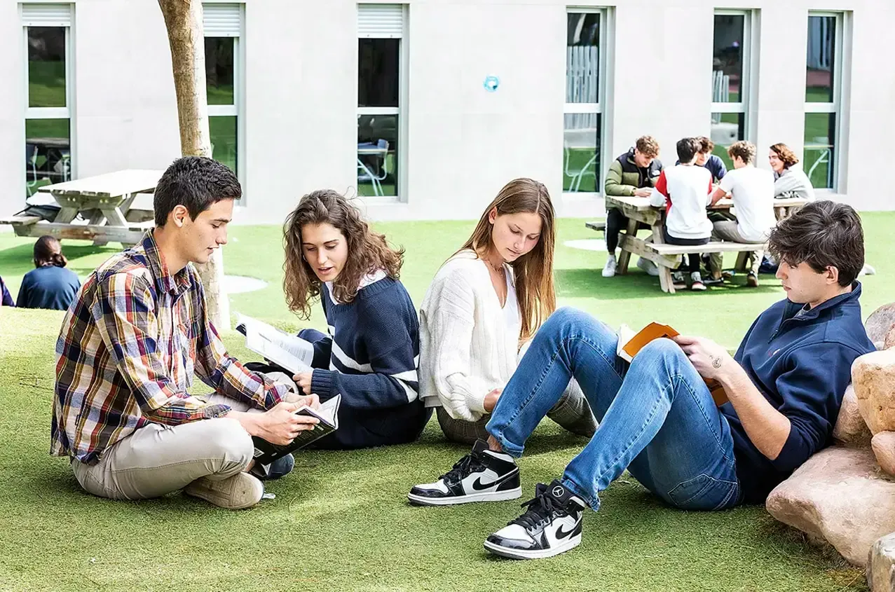 A group of young people are sitting on the grass reading books.