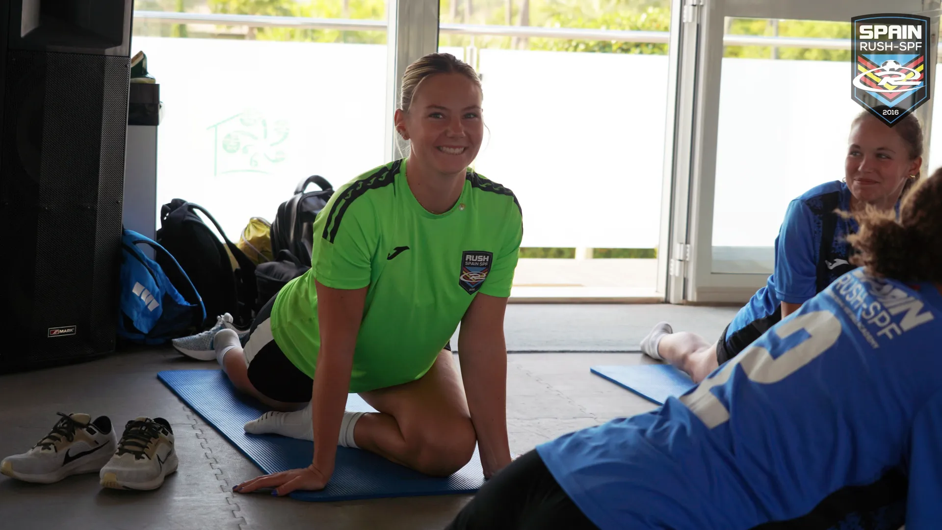 A female soccer player sitting on a yoga mat in a gym.