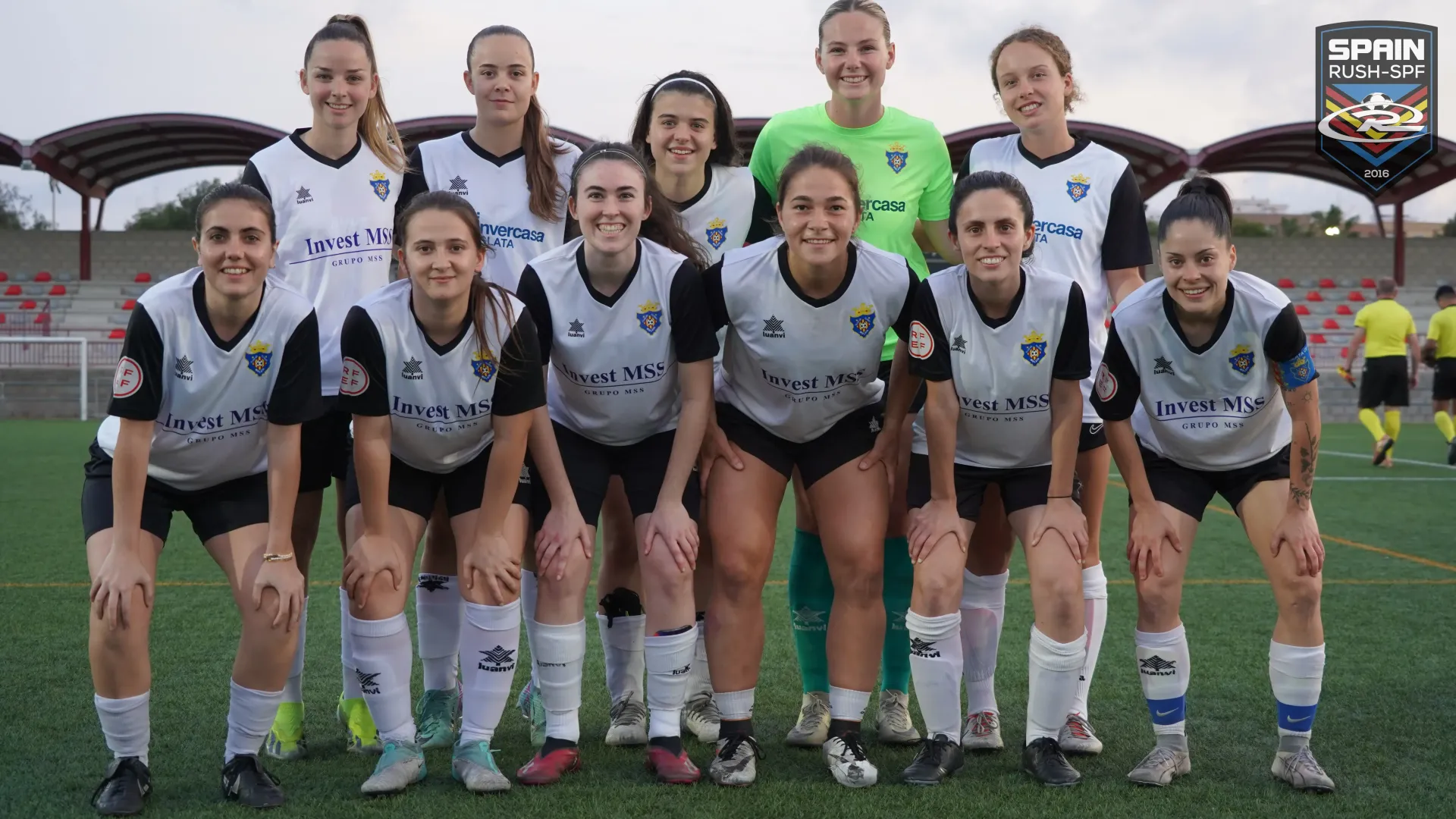 A group of female soccer players are posing for a team photo on a field.