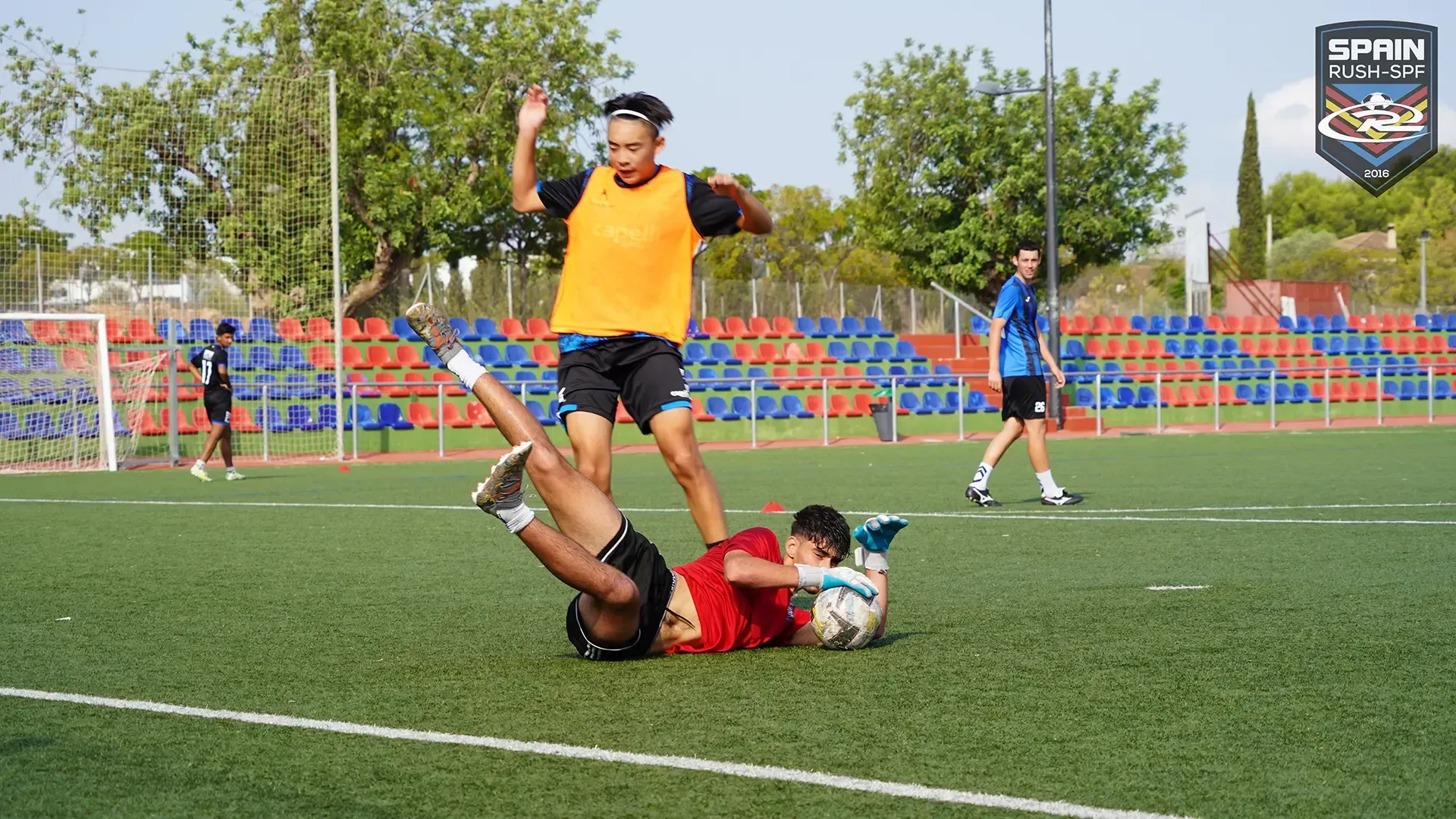 A goalkeeper stopping soccer ball shot on a field.
