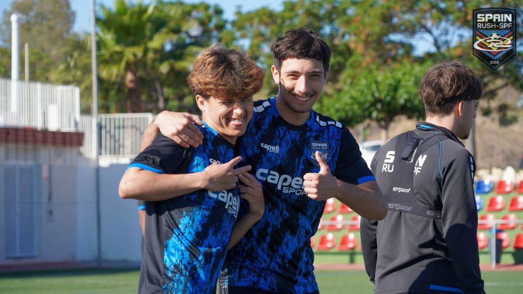 Two young spain rush-spf players are posing for a picture on a soccer field.