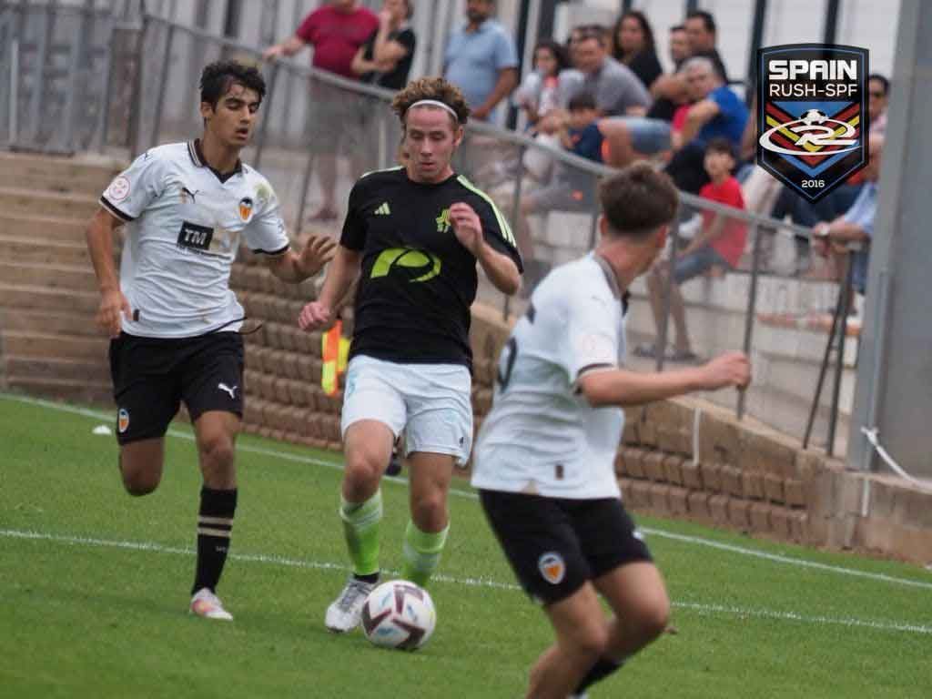 James Forbes dribble a soccer ball down a soccer fields surrounded by two defenders in white