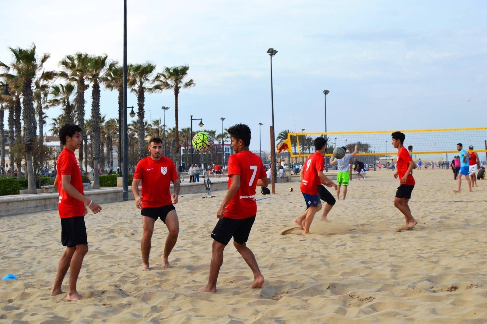 A group of young men are juggling a soccer ball on a sandy beach.