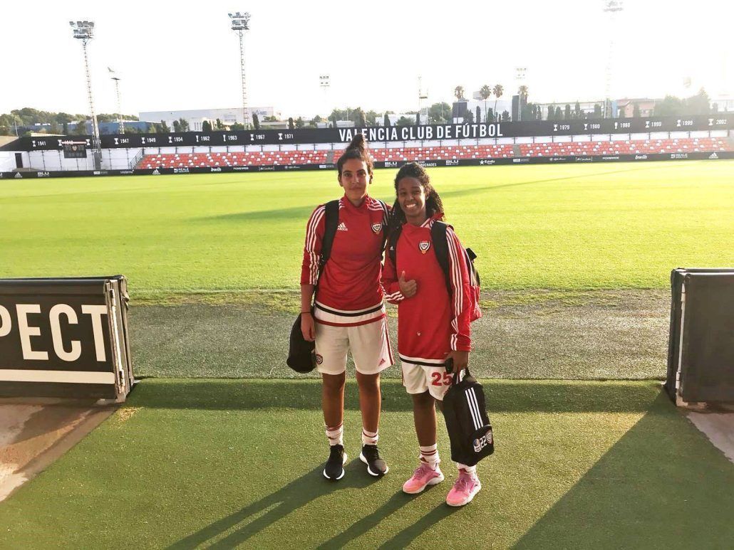 Two young girls are posing for a picture on a soccer field.