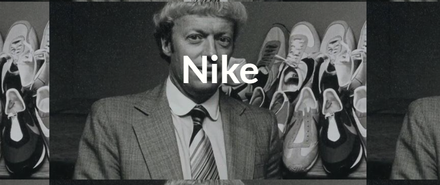 A man in a suit and tie is standing in front of a row of Nike shoes.