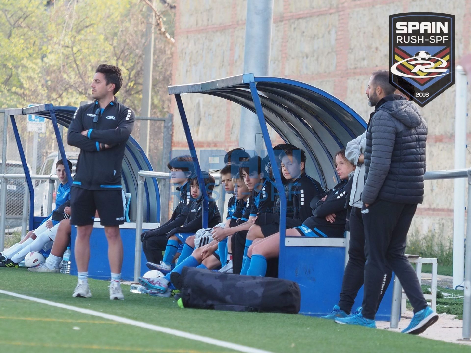 A group of soccer players are sitting in a dugout on a field.