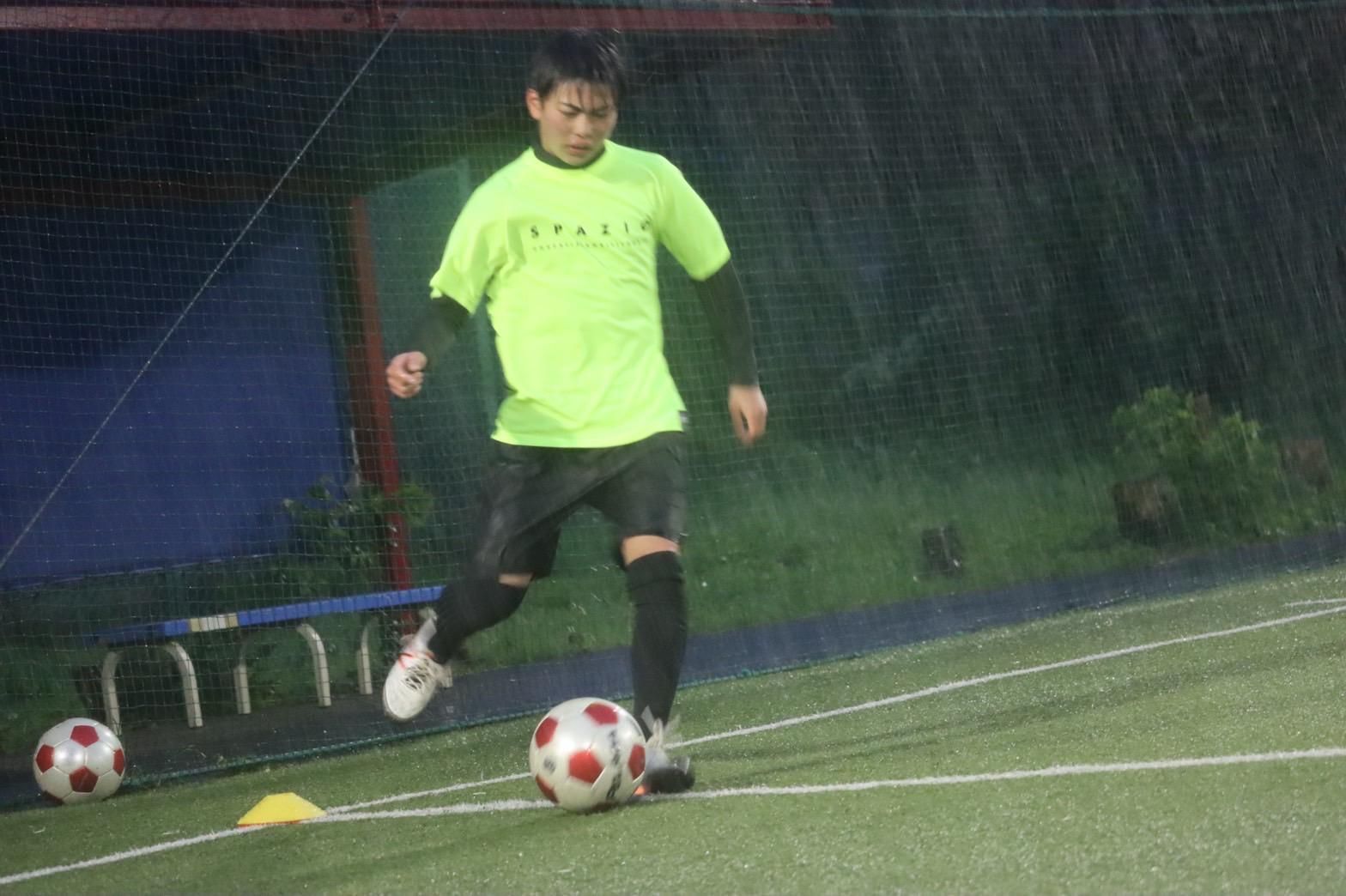 A man is kicking a soccer ball on a field in the rain