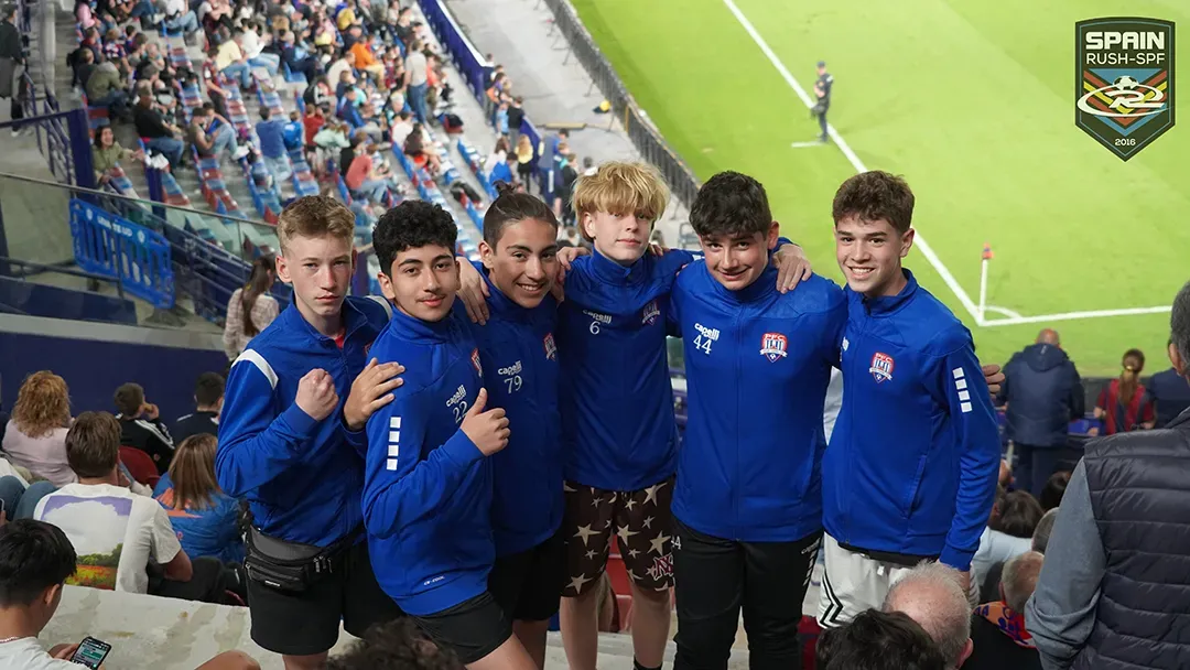 A group of young soccer players are posing for a picture in front of a soccer field.