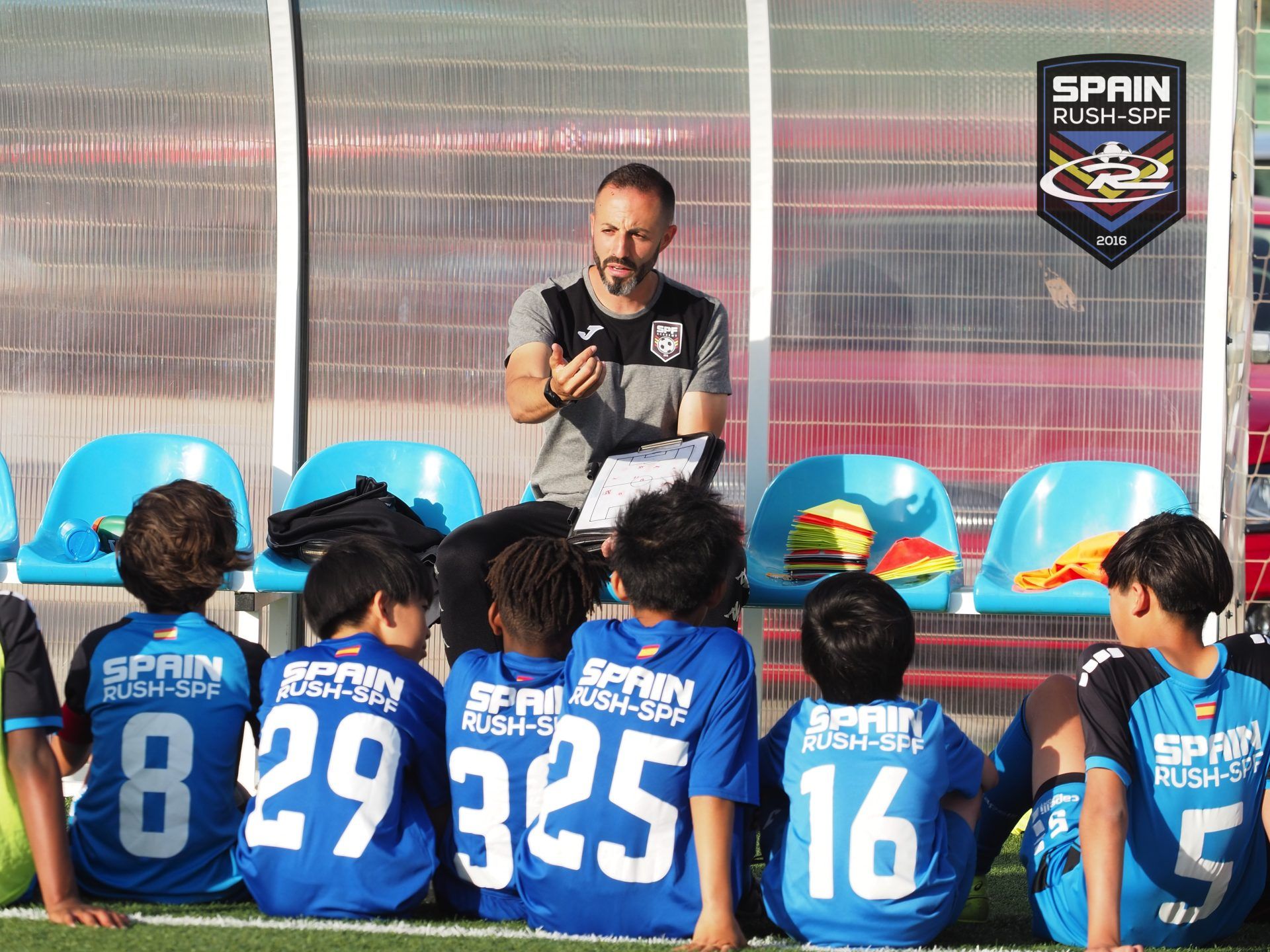 A man is talking to a group of young soccer players sitting on the field.