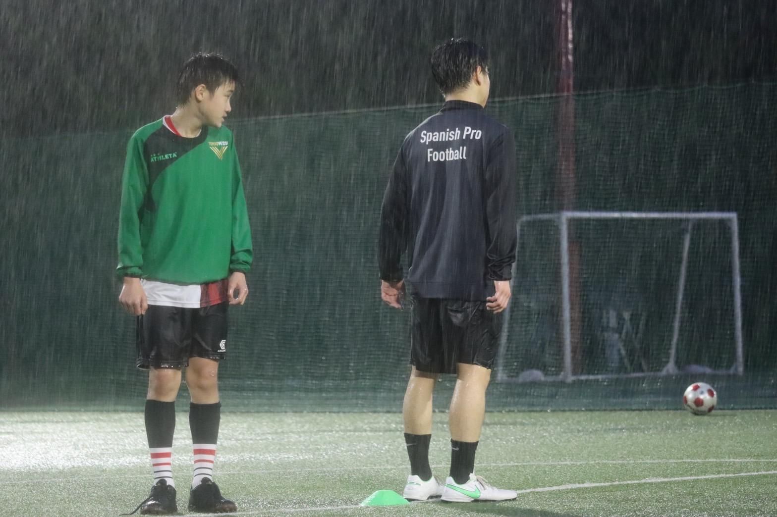 Two men are standing on a soccer field in the rain.