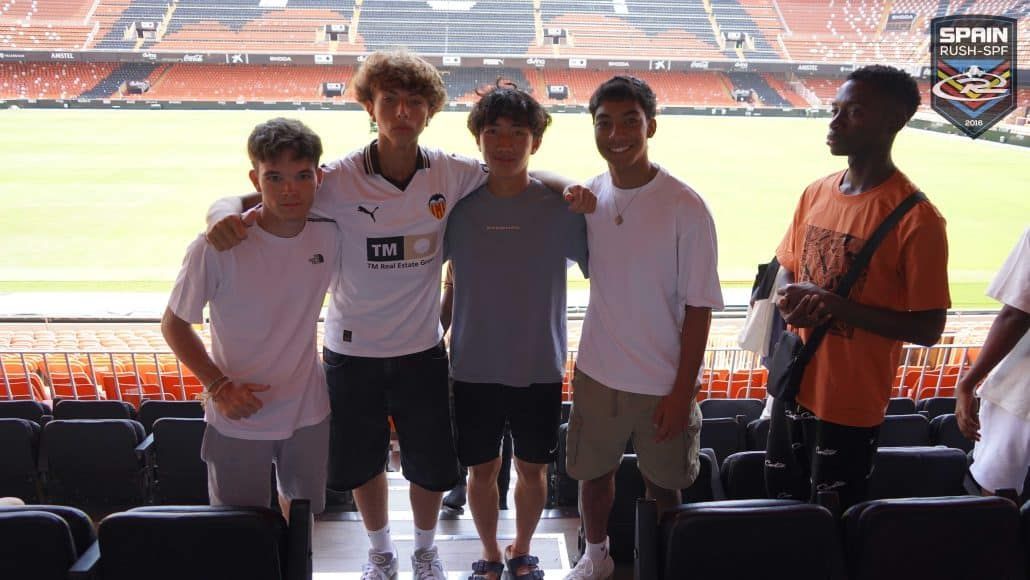 Five young male soccer players posing together at a stadium, with one wearing a Valencia CF jersey.